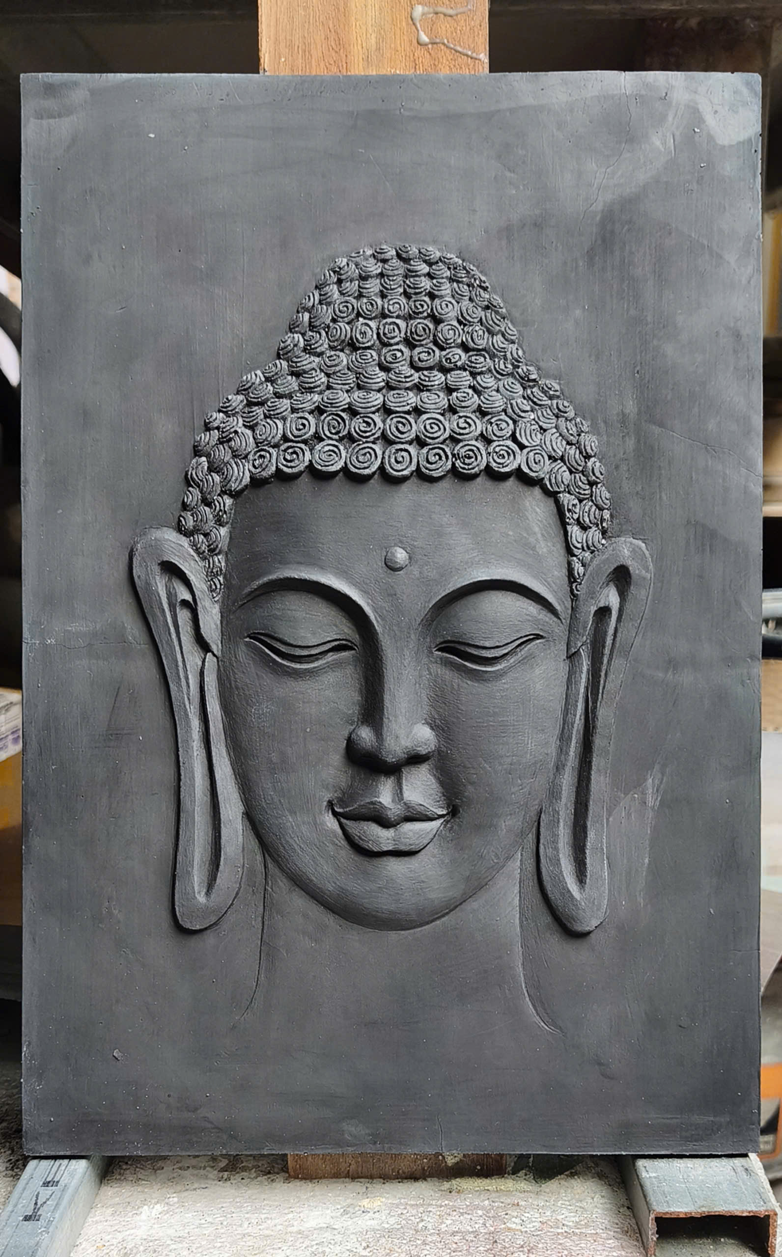 A Buddha wall relief in a deep charcoal finish, on a stand