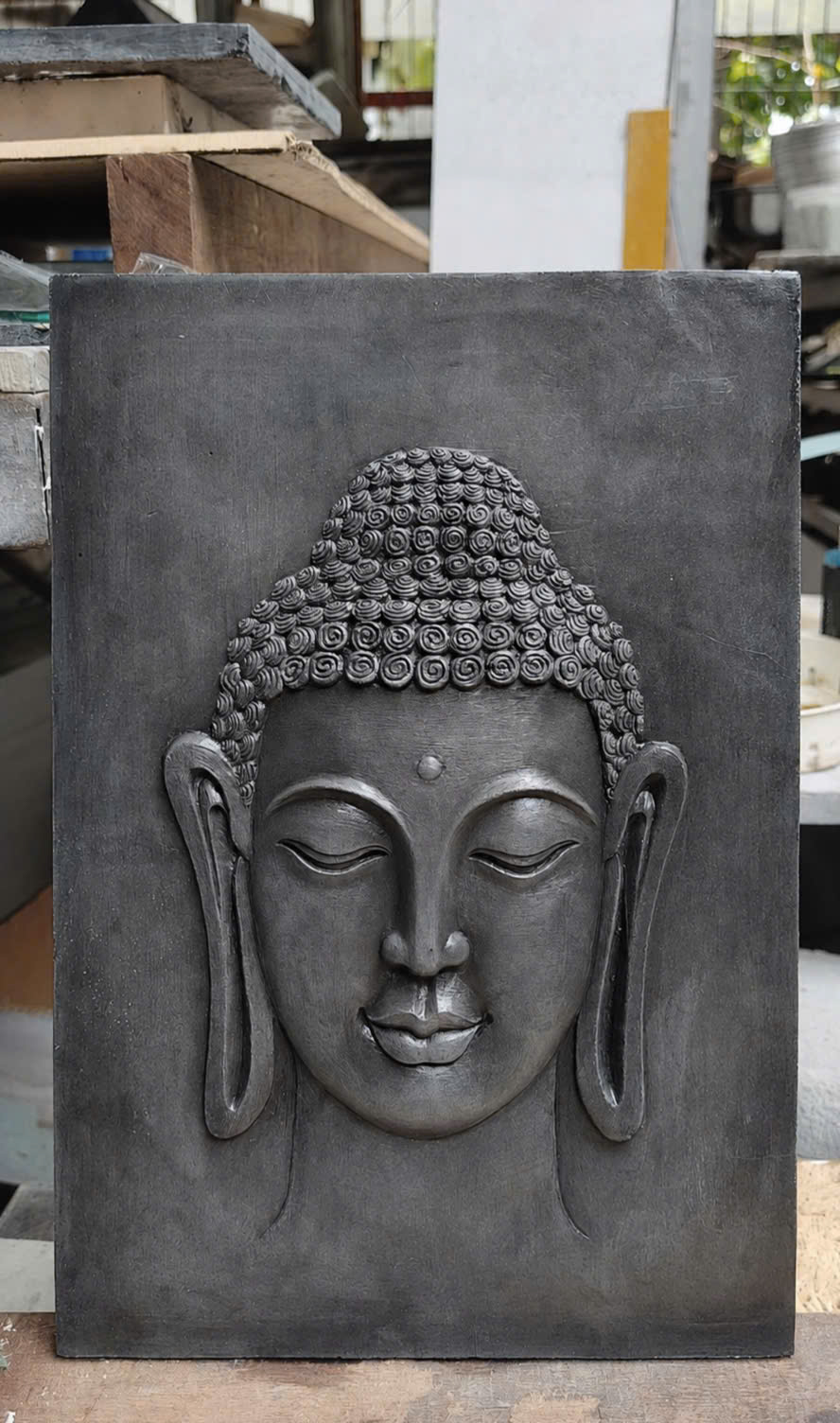A Buddha wall relief in a dark finish, standing in the workshop